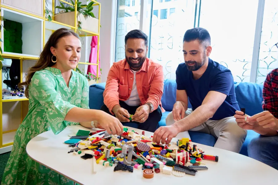 Adults building together with colorful LEGO bricks at a table - official LEGO lifestyle photo
